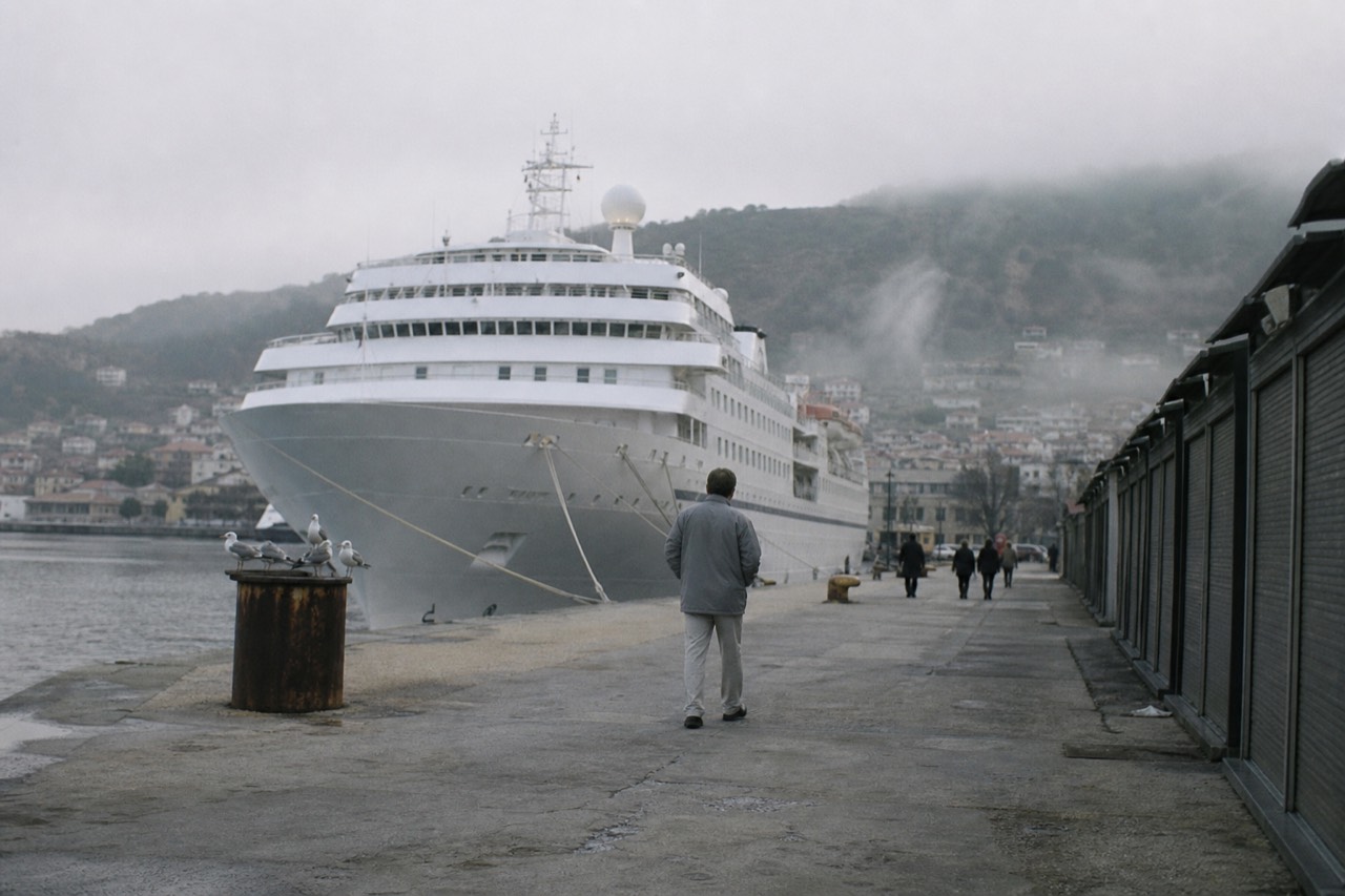 Cruise ship docked at the Ensenada port with the town and hills behind, no text, no logos, no people