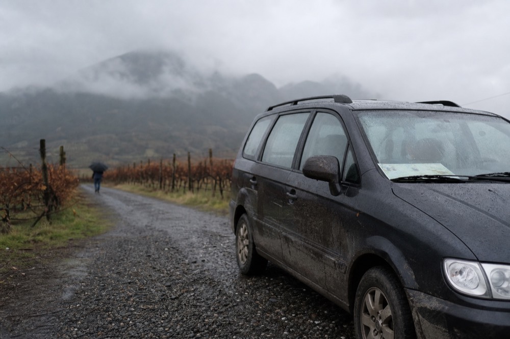 Shared tour van parked on a gravel road beside vineyard rows, no text, no logos, no people