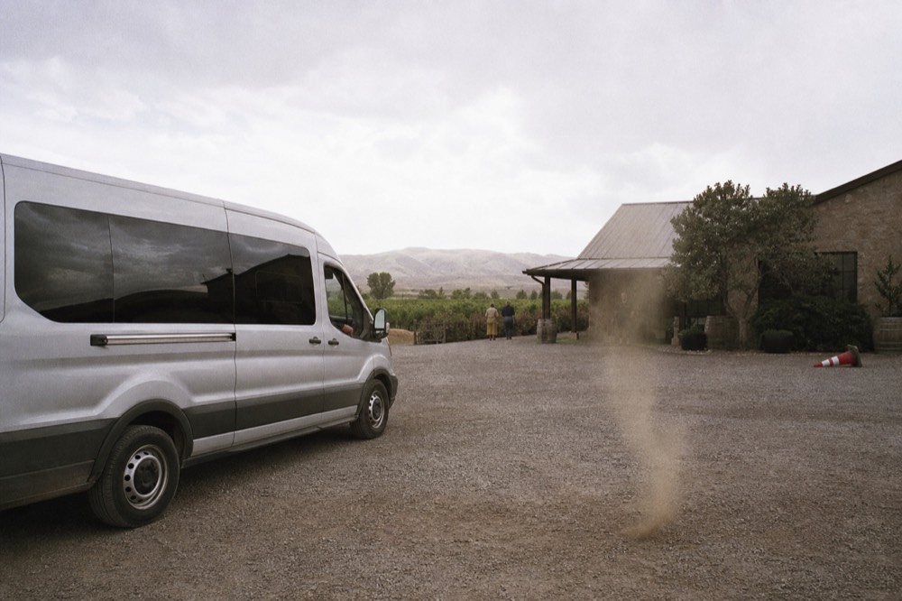 A tour van parked on a gravel lot beside a winery building, no text, no logos, no people