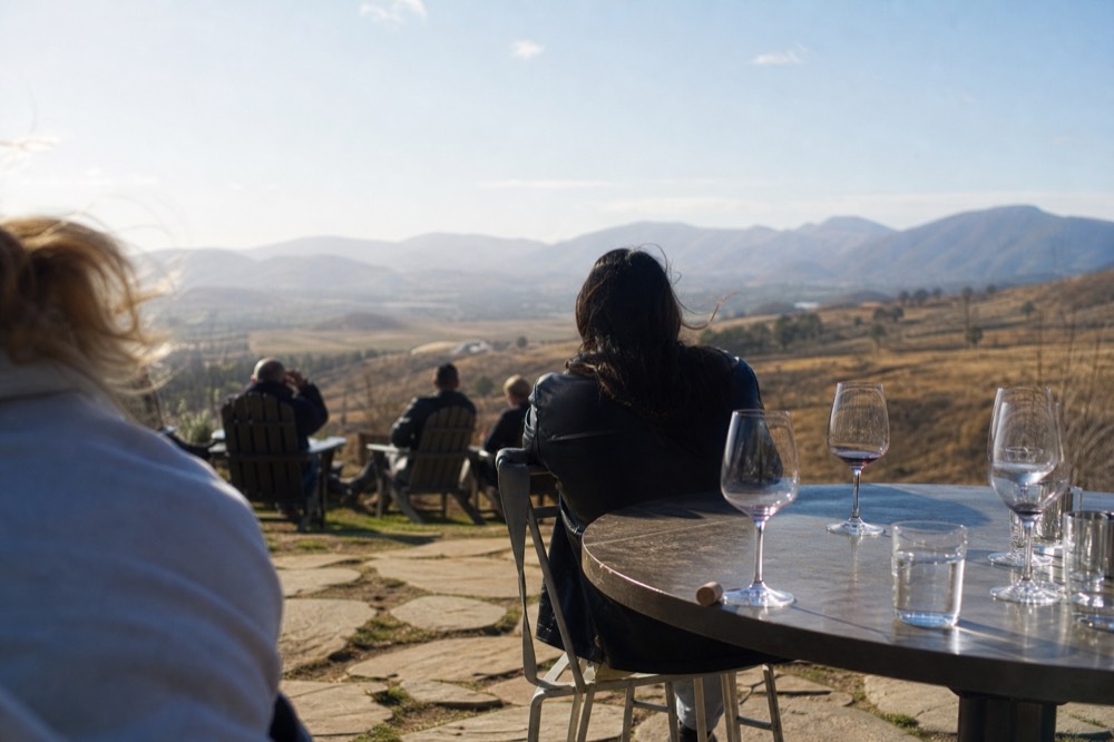 Outdoor tasting table set with wine glasses beside an open valley view, no text, no logos, no people.