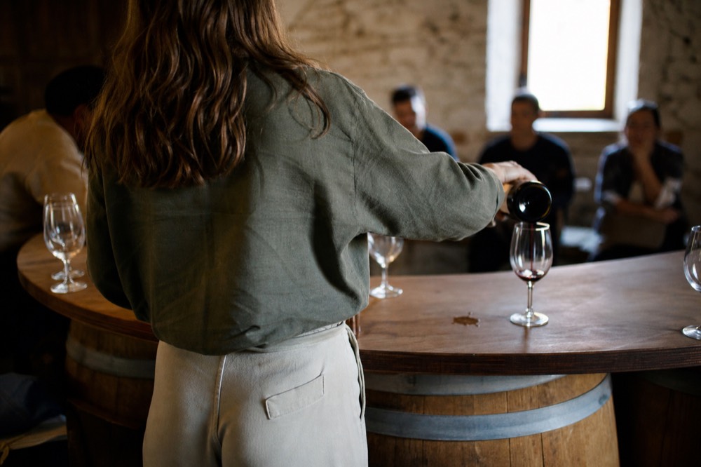 A guide pouring wine for guests at a rustic valley tasting counter, no text, no logos, no people.