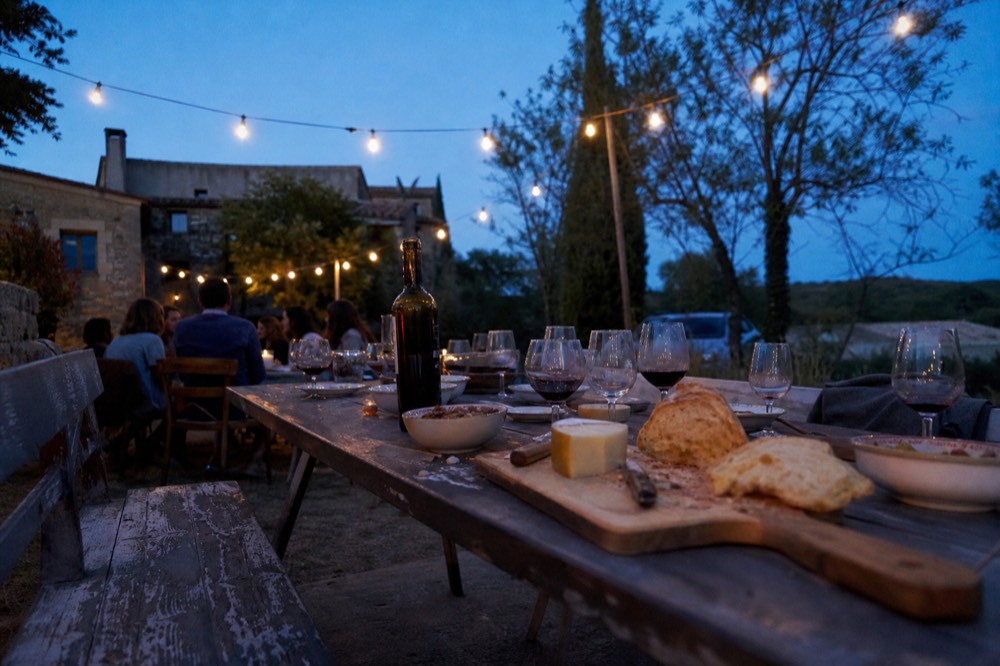 Rustic outdoor dining table with bread, cheese and glasses of red wine under string lights, no text, no logos, no people