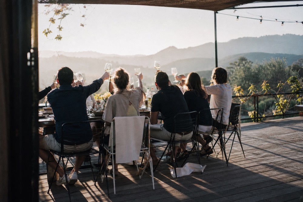 Group of travelers toasting with wine glasses around a long table on a terrace, no text, no logos, no people