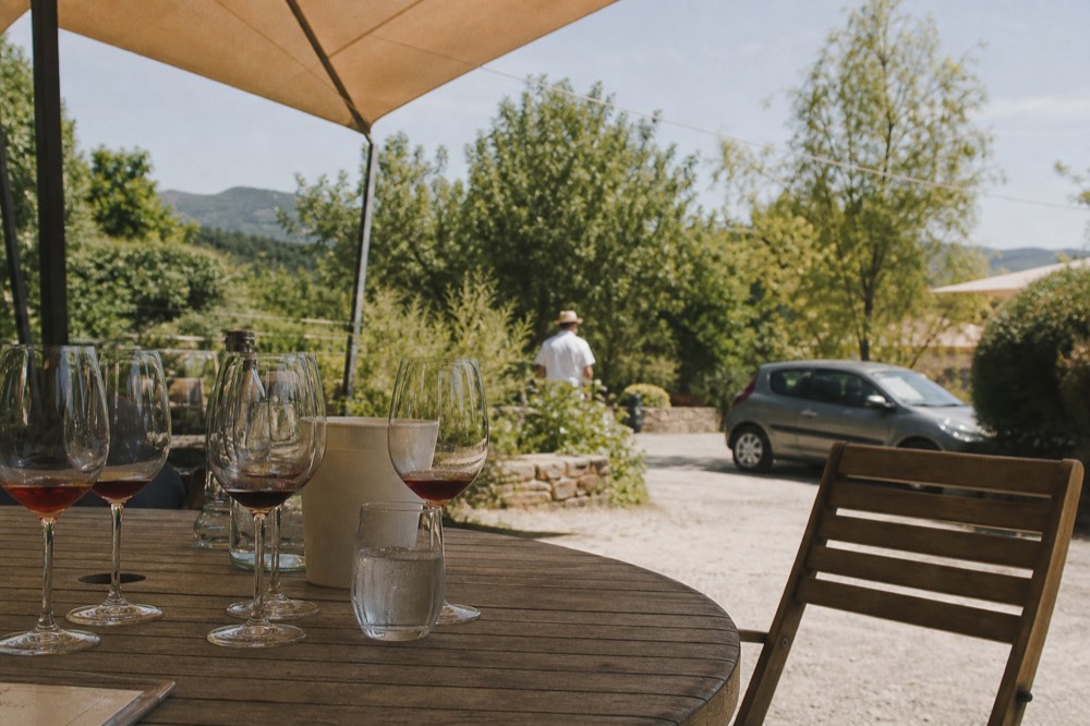 A shaded outdoor tasting table set with wine glasses on a warm day, no text, no logos, no people