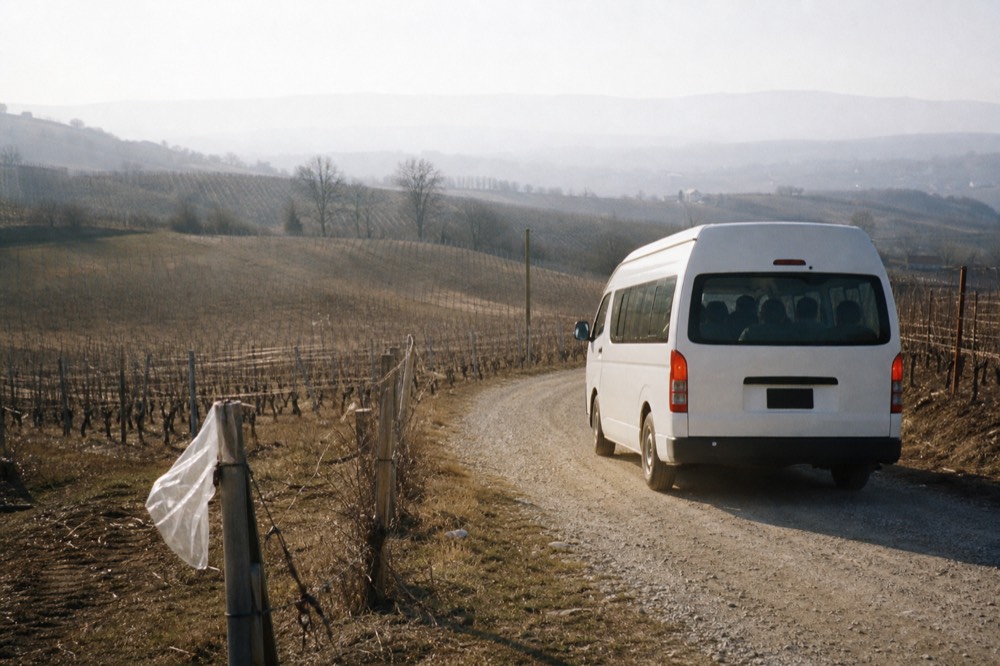 A van winding along a rural road between vineyards in Valle de Guadalupe, no text, no logos, no people.