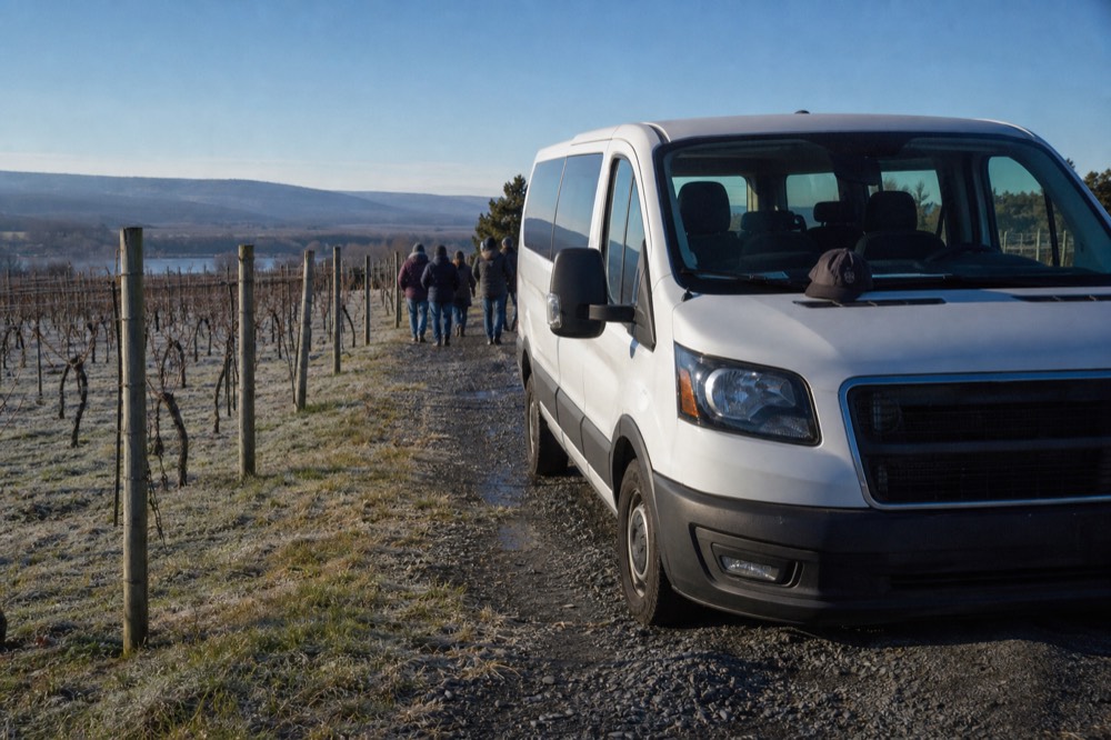 A van parked on a gravel road beside vineyard rows ready for a tour pickup, no text, no logos, no people.