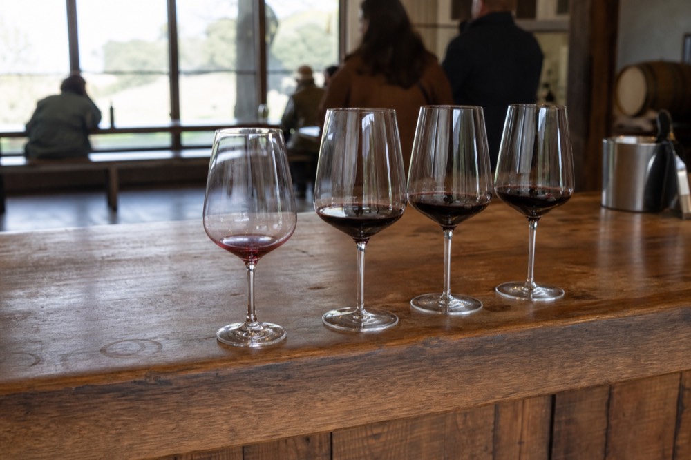 A tasting flight of red wines on a wooden winery bar, no text, no logos, no people