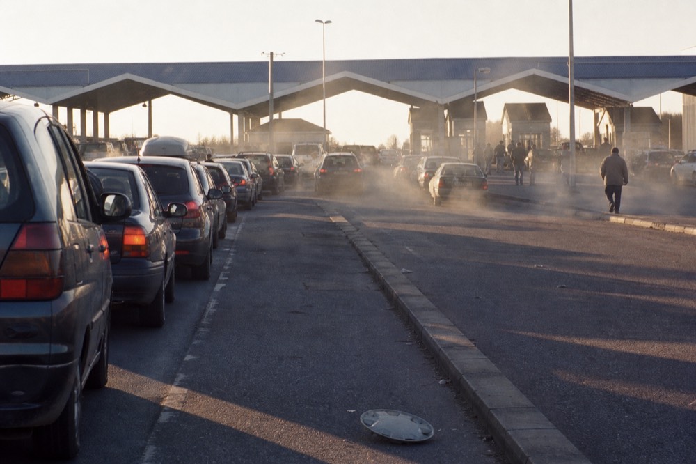 A line of cars waiting at a border checkpoint station in late afternoon light, no text, no logos, no people